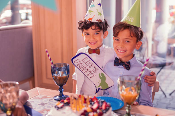 istock Positive boys holding lets party sign and smiling while sitting with cake 1047182930