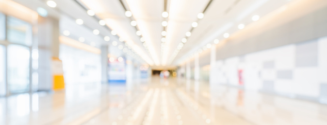 Blurred bokeh panoramic banner background of exhibition hall or convention center hallway. Business trade show event, modern interior architecture, or commercial tradeshow conference seminar concept