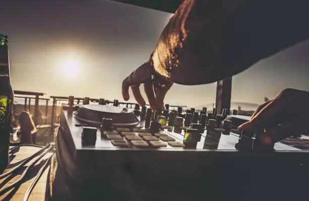 Close up of unrecognizable DJ playing music on turntable during summer beach party at sunset.