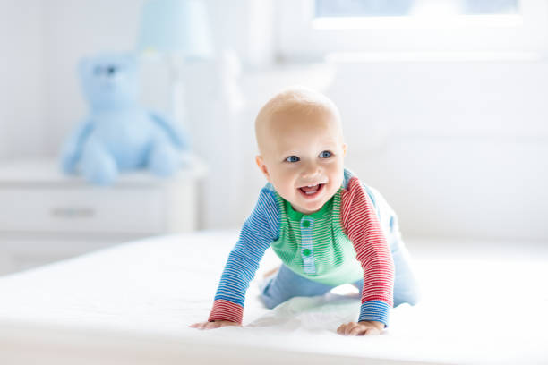 Baby boy crawling on bed Baby boy crawling on bed. Little child playing in white sunny bedroom. Infant kid learning to crawl. Nursery for children. Textile, clothing and bedding for kids. Family morning at home. cute baby laughing stock pictures, royalty-free photos & images
