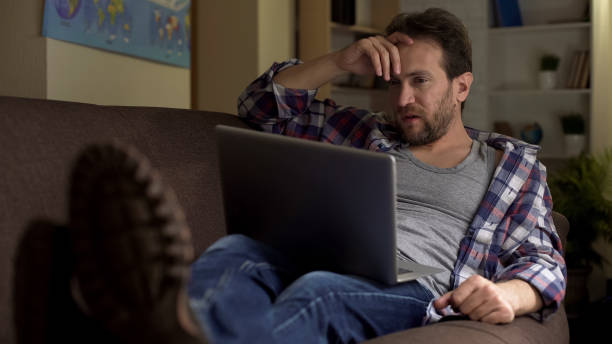 istock Guy sitting on sofa, looking at laptop, angry with received news, bitterness 1047209530