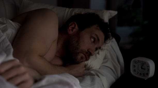 istock Annoyed guy in bed unable to fall asleep, looking angrily at clock, insomnia 1047212472