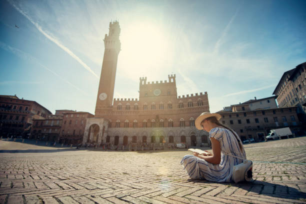 niña adolescente leyendo un libro sobre piazza del campo, siena, italia - torre del mangia fotografías e imágenes de stock