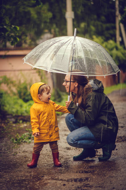 istock Mother and son in raincoats under umbrella in rain 1047239180