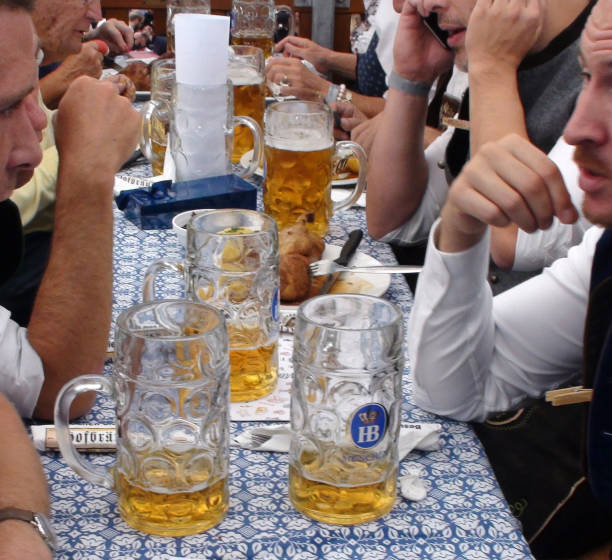 People Having A Drink At Munich Oktoberfest Scene In Germany Europe Scene Of Advertisement Sign, Lot Of People Wearing Bavarian Traditional Oktoberfest Costumes Sitting Down In A Beer Tent, Looking Around, Talking To One Another, Laughing, Holding Giant Beer Mug And Drinking Beer During Annual Oktoberfest In Munich Germany Europe large german beer steins stock pictures, royalty-free photos & images