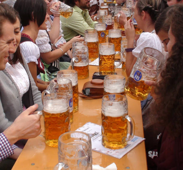 Oktoberfest In Munich Germany Plus People Drinking Beer With Giant Beer Mug Scene During The Day Scene Of Advertisement Sign, Lot Of People Wearing Bavarian Traditional Oktoberfest Costumes Sitting Down In A Beer Tent, Looking Around, Talking To One Another, Laughing, Holding Giant Beer Mug And Drinking Beer During Annual Oktoberfest In Munich Germany Europe large german beer steins stock pictures, royalty-free photos & images