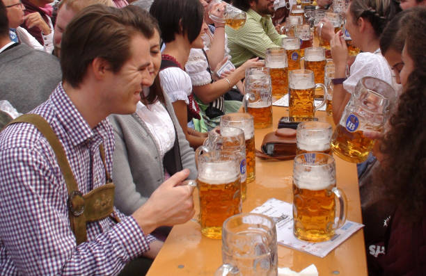 Oktoberfest In Munich Germany Plus People Drinking Beer With Giant Beer Mug Scenery During The Day Scene Of Advertisement Sign, Lot Of People Wearing Bavarian Traditional Oktoberfest Costumes Sitting Down In A Beer Tent, Looking Around, Talking To One Another, Laughing, Holding Giant Beer Mug And Drinking Beer During Annual Oktoberfest In Munich Germany Europe large german beer steins stock pictures, royalty-free photos & images