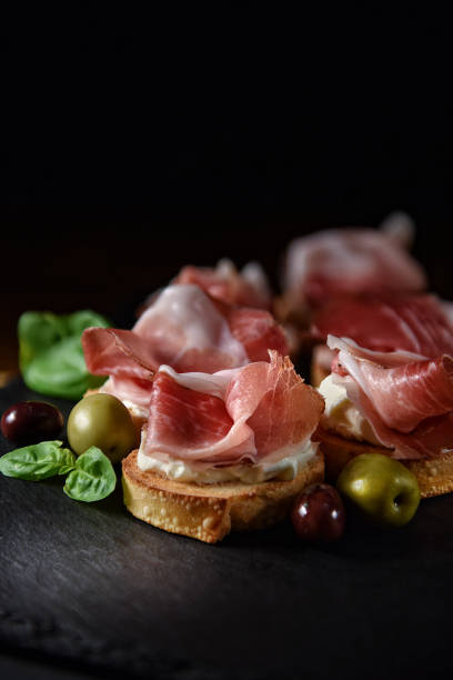 Italian Prosciutto Canapes Italian smoked prosciutto canapes with green and black olives and basil herb garnish shot against a black background with generous accommodation for copy space. tapas photos stock pictures, royalty-free photos & images
