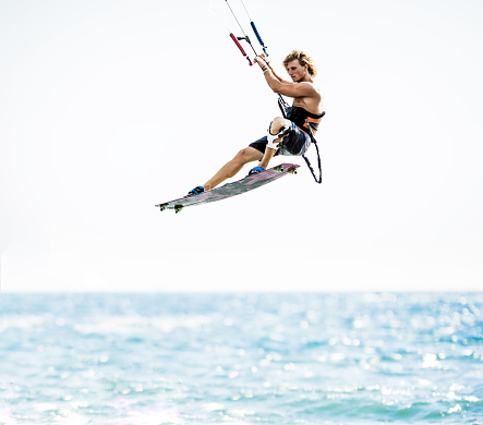 Young man flying with kiteboard above the sea.