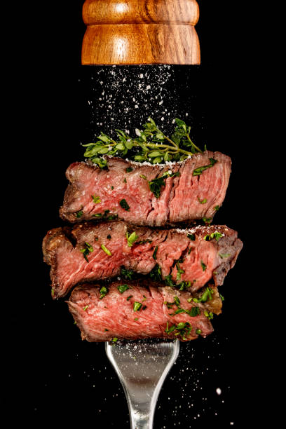 Sliced beef steak from grill on a fork. Salt is strewing from wooden mill stock photo