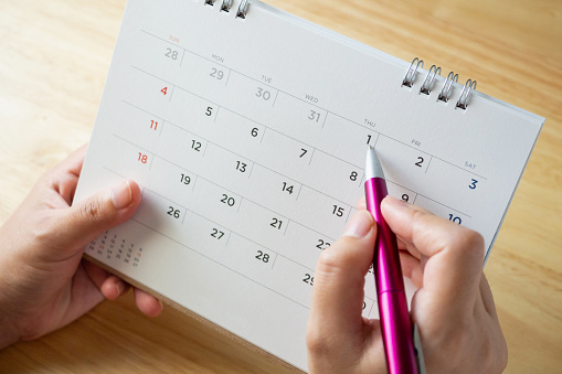 calendar page with female hand holding pen on desk table