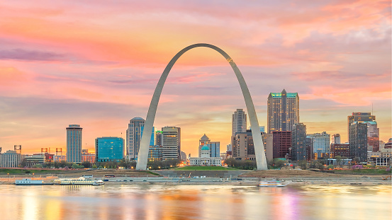 St. Louis, MO, USA - August 10, 2018: A view from the Mississippi River of a dark St. Louis skyline with the Gateway Arch. A sunset/sunrise, after a rainstorm, lights up the sky with colorful clouds.