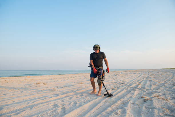 hombre con un detector de metales en una playa de arena de mar - lost beach fotografías e imágenes de stock