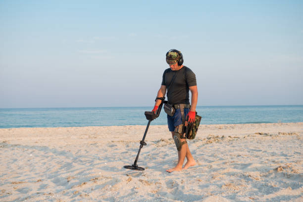 homem com um detector de metais em uma praia de areia do mar - ancient weapon audio - fotografias e filmes do acervo