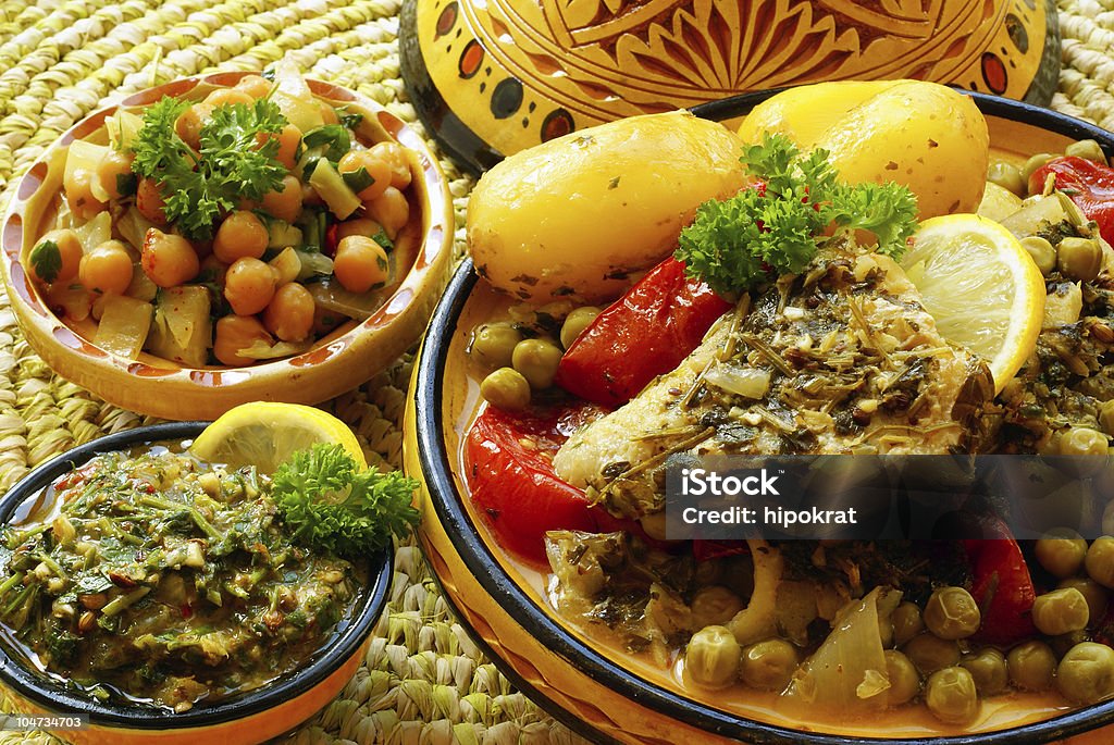 Close-up image of several bowls of Moroccan foods Moroccan fish marinated in Chermoula relish, simmered with new potatoes, peas and tomatoes and served with warm chickpeas salad Fish Stock Photo