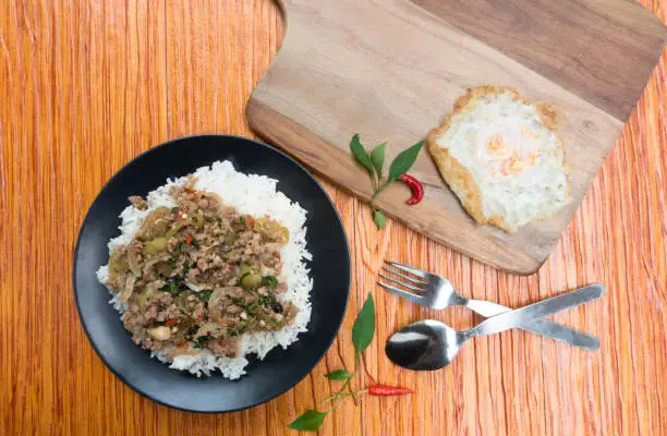 Photo of Salted pork with chili & Basil leaves in black plate on wood table, space for text input.