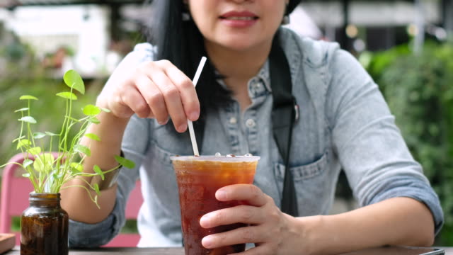asian woman stirring ice tea at coffee shop in sunny day.summer drink
