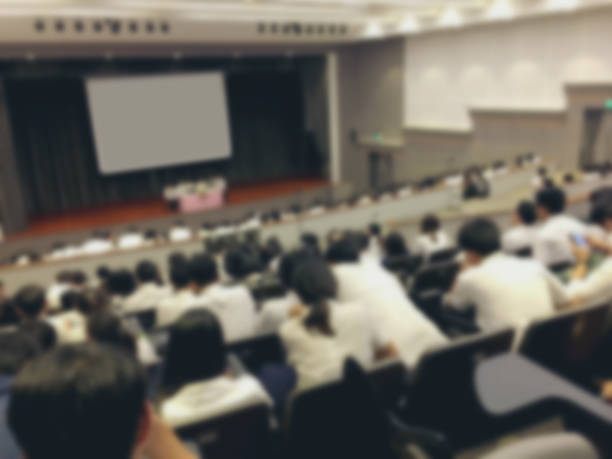 istock Education concept, Abstract blurred background image of students and business people  studying and discuss in large hall profession seminar with screen and projector for showing information. 1047398958