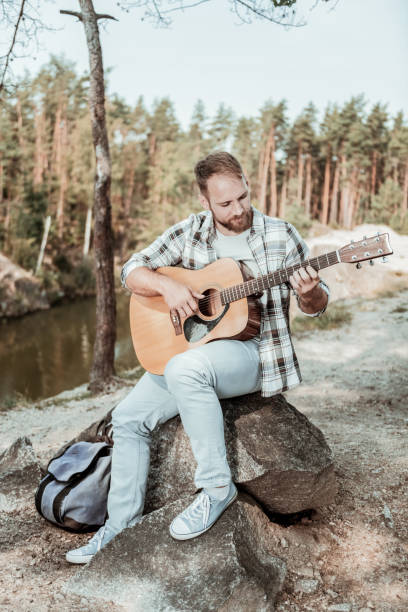 istock Creative handsome young man hiking in forest with his backpack playing the guitar 1047407186