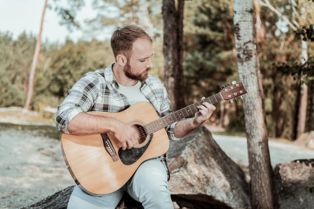 istock Handsome blonde-haired bearded man feeling inspired while playing the guitar 1047407192