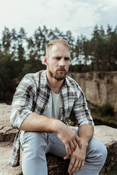 istock Handsome blonde-haired model posing for photo while sitting on rock near canyon 1047407246
