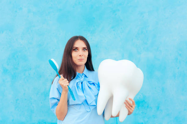 Funny Woman Holding Oversized Tooth in Dentist Concept Image Cute girl with big wisdom molar or implant mock-up model tooth enamel stock pictures, royalty-free photos & images