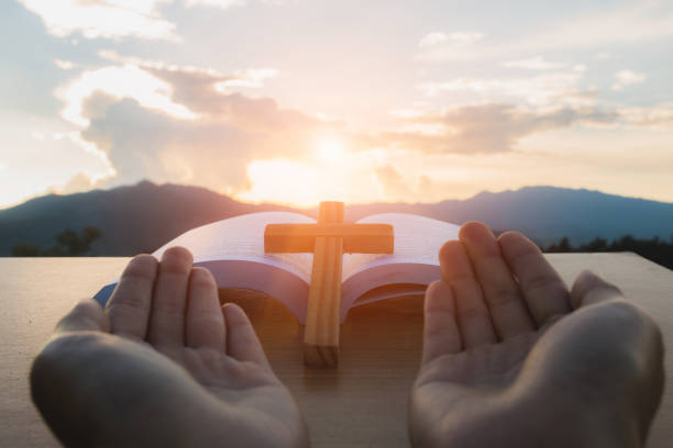 istock Human hands open palm up worship, open Bible, script in blur with focus on palm cross,  Eucharist Therapy Bless God Helping Repent Catholic Easter Lent Mind Pray. 1047424296