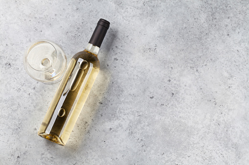 White wine bottle and glass lying on stone backdrop. Top view with space for your text