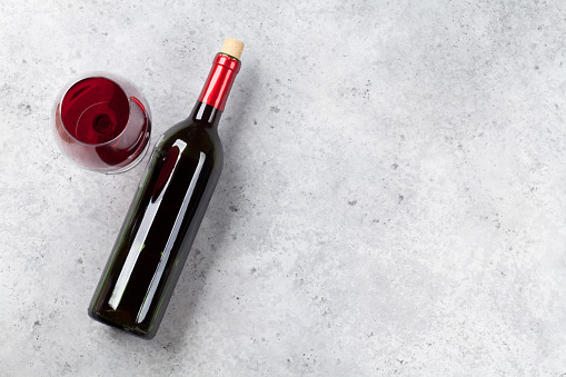 Red wine bottle and glass lying on stone backdrop. Top view with space for your text