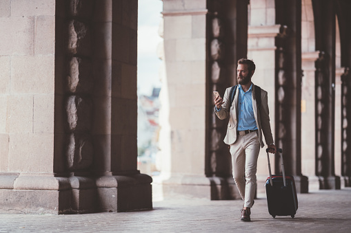 Businessman pulling suitcase and texting on smartphone