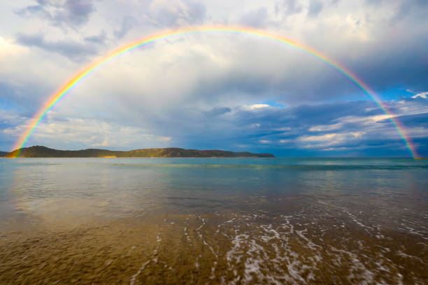 istock Rainbow over ocean and beach against cloudy blue sky 1047448474