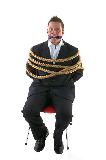 Businessman tied up with rope and gagged with his own tie, a look of fear in his eyes. Isolated on a white background.