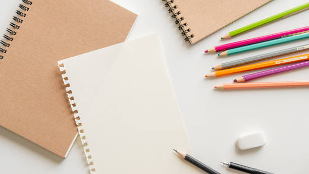 istock blank paper with spiral notebook, pencil, eraser and color pencil on white background. 1047465872