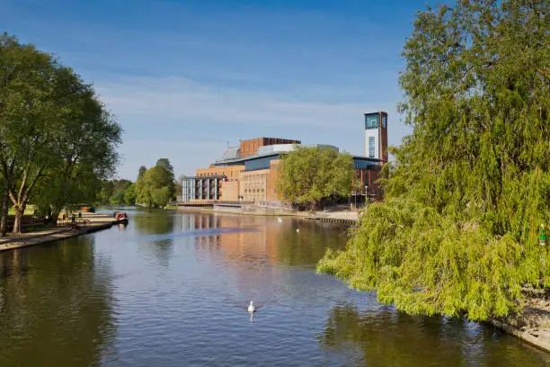 The Royal Shakespeare Theatre, home of the Royal Shakespeare Company, reflecting in the River Avon, with a swan in the foreground.