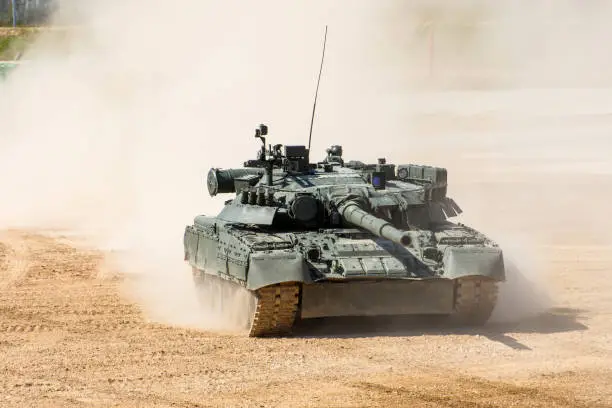 Photo of Powerful military tank rides at a high speed along the dusty field.