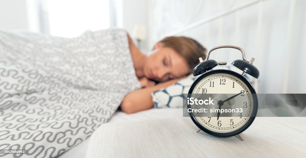 Analog alarm clock. Woman sleeping in bed Young woman is sleeping in her bed. Alarm clock in the foreground Change Stock Photo