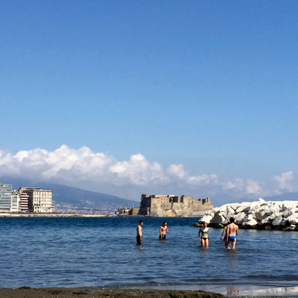 Naples, Italy - April 13, 2017: View of the city of Naples and the waterfront with young people at the sea in the springtime. Ovo Castle in the background.