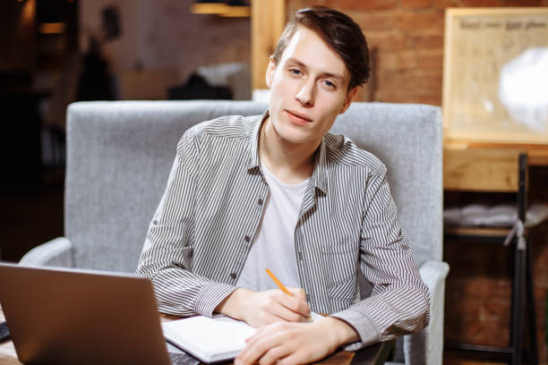 istock Young male student writes information in a notebook, prepare for lectures in University campus, hipster businessman working on laptop computer, writing business plan while sitting in cafe. 1047493850