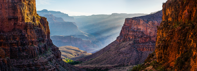 Panoramic vista down the Bright Angel Trail to the green oasis of Indian Garden and the early morning rays of sunlight illuminating the North Rim of the Grand Canyon National Park, Arizona, USA.