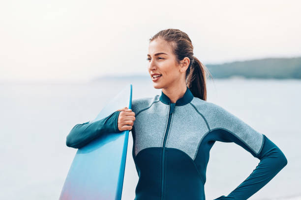 istock Female surfer standing with arm around her board 1047499234