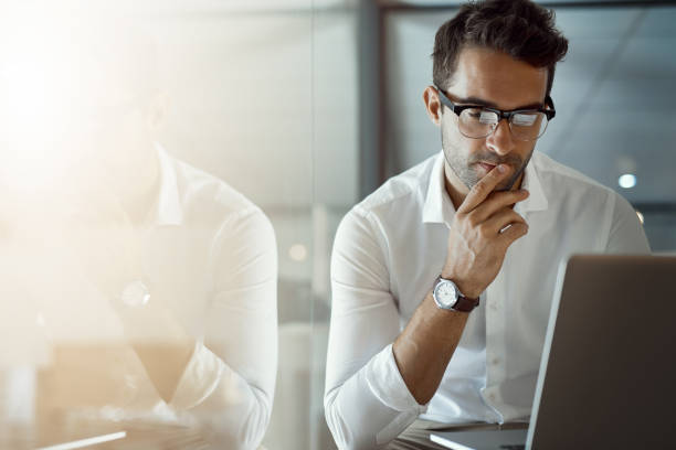 Mmm...I wonder Cropped shot of a handsome young businessman looking thoughtful while working on his laptop in the office reflecttion stock pictures, royalty-free photos & images