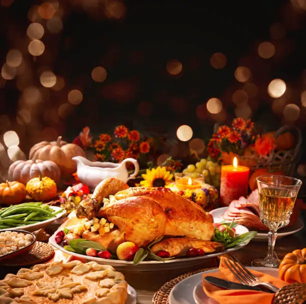 Thanksgiving dinner. Roasted turkey garnished with cranberries on a rustic style table decoraded with pumpkins, vegetables, pie, flowers, and candles