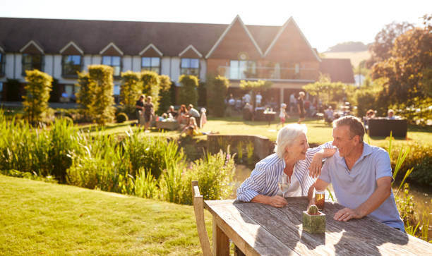 coppia senior seduta a tavola che si gode un drink estivo all'aperto al pub - giardino di birra foto e immagini stock
