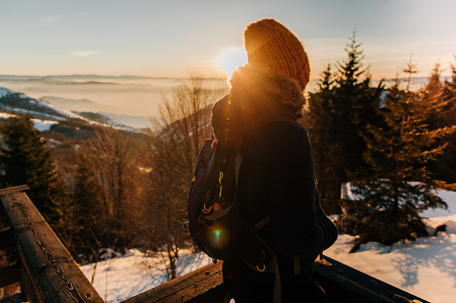 Photo of a young woman enjoying stunning view from the top of the mountain during sunset