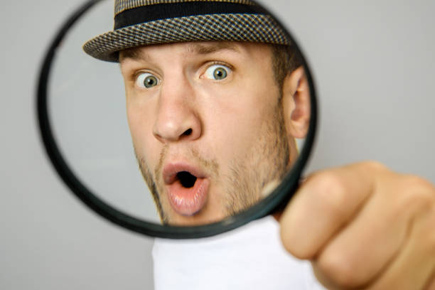 istock Astonished man looking through a magnifying glass on gray background 1047519238