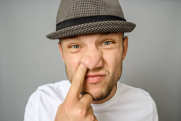hombre de escoger su nariz. el emotivo retrato de hombre con sombrero y camiseta en blanco. fondo gris - picking nose fotografías e imágenes de stock