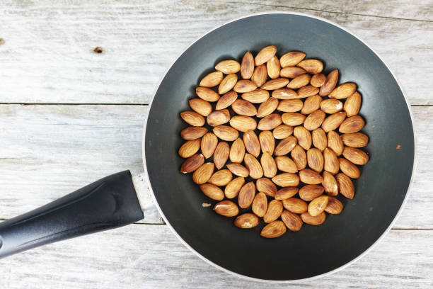 istock Roasted almonds in dark pan against rustic wooden background 1047520850