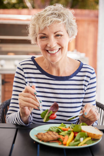 istock Senior white woman eating lunch at a table outside, vertical 1047524228