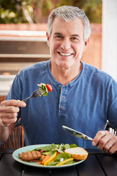 istock Senior white man eating lunch at a table outside, vertical 1047524396