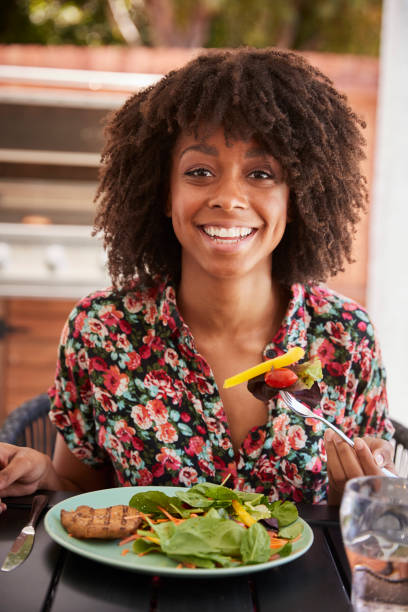 istock Young black woman eating lunch at a table outside, vertical 1047524648